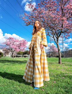 Woman in long yellow dress under pink cherry blossoms on sunny day