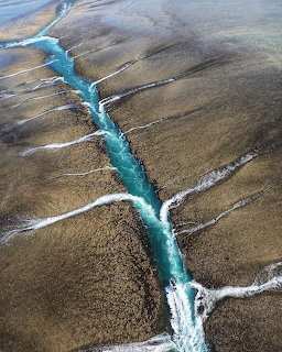 Aerial view of a bright turquoise channel flowing through exposed brown reef flats