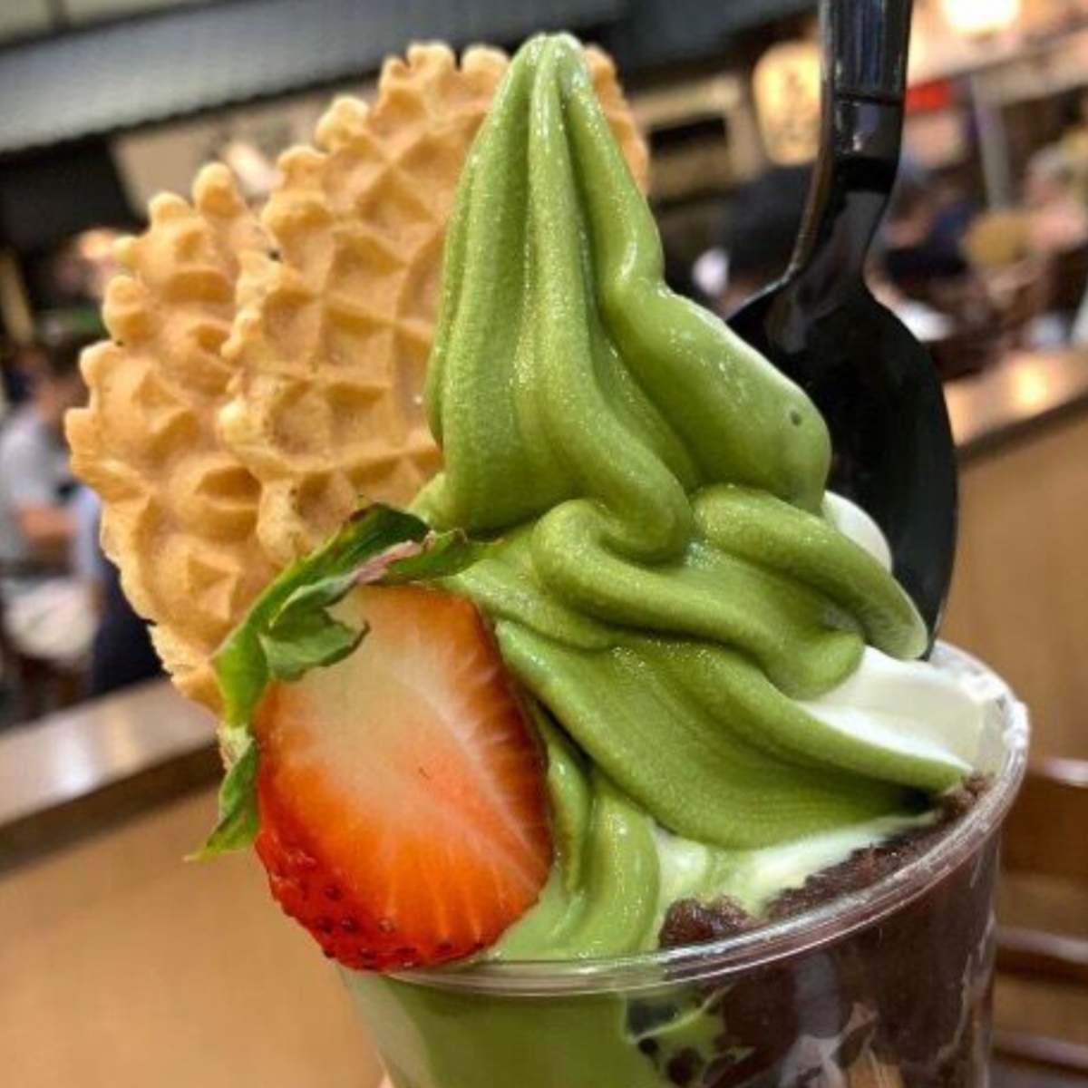 Matcha soft serve dessert in a cup with strawberry, red bean, and waffle cookie