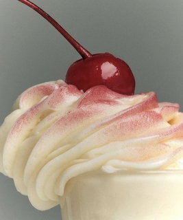 Swirled soft serve ice cream topped with a red maraschino cherry on a stem