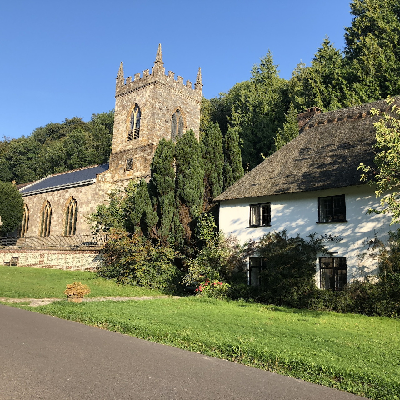 Stone church with tower next to white thatched cottage on village green surrounded by trees