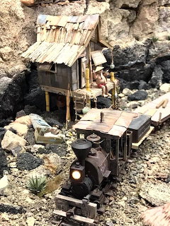 Miniature steam train on rocky tracks beside an old wooden shack