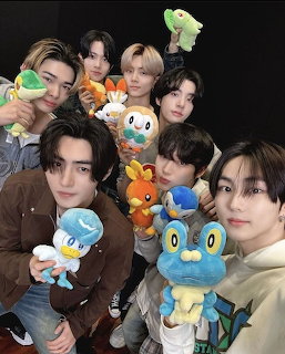 Group of young men smiling and holding colorful Pokemon stuffed animals in a group photo