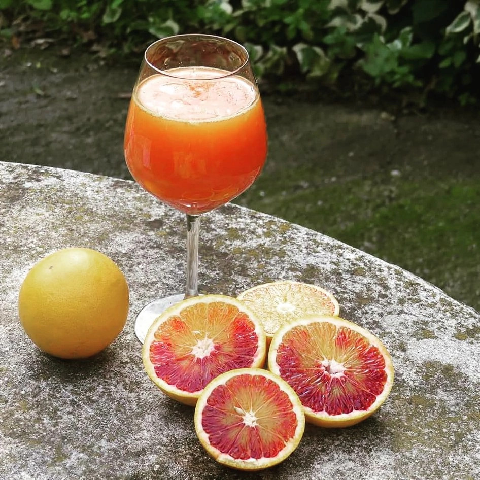 Glass of blood orange juice with whole and sliced blood oranges on a stone table
