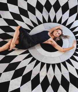 Woman in black dress on bold black and white geometric patterned floor with radiating diamond shapes