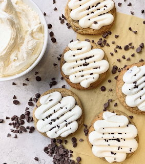 Frosted cookies with white cream cheese icing and mini chocolate chips on parchment paper, overhead view