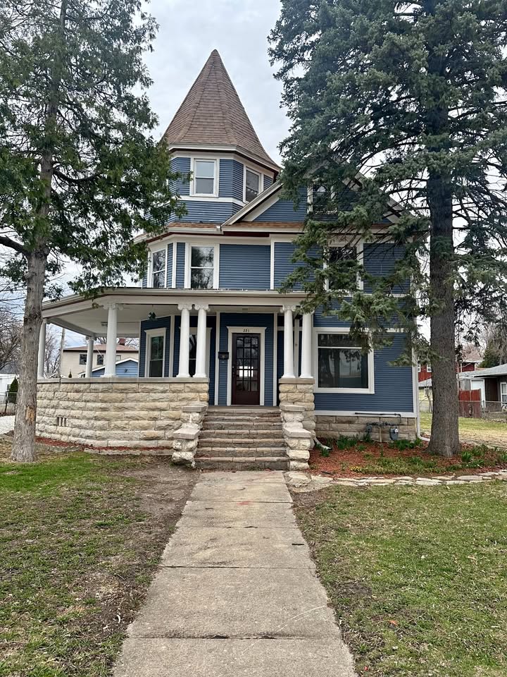 Victorian-style house with wraparound porch, front steps, and tall trees