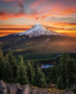 Snow-capped Mt. Hood at sunset with colorful sky, evergreen forest, and mountain lake in foreground