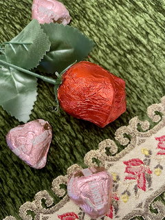 Foil-wrapped chocolate roses in red and pink with green leaves on embroidered lace and green velvet