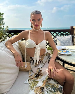 Woman in white crop top and tropical skirt sitting on outdoor terrace with ocean background