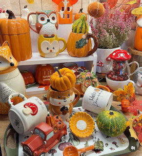 Collection of autumn-themed ceramic decor with pumpkin mugs, owl and fox figurines, and fall leaves