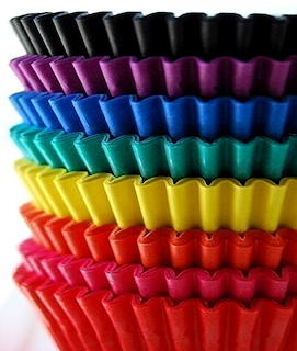 Stack of colorful ruffled paper cupcake liners in rainbow colors from red at bottom to black at top