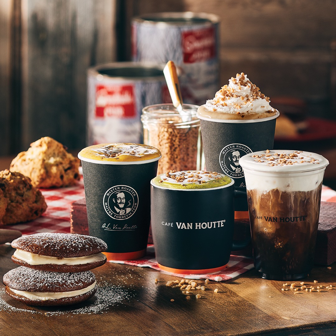 Various coffee beverages in branded cups with cookies and pastries on wooden table