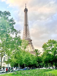 Eiffel Tower viewed through green trees in Paris park with cloudy sky