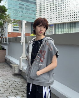 Young man in gray sleveless hoodie posing on urban rooftop with city buildings behind