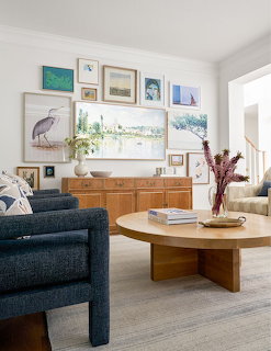 Bright living room with a blue armchair, wooden coffee table, sideboard, and gallery wall art.