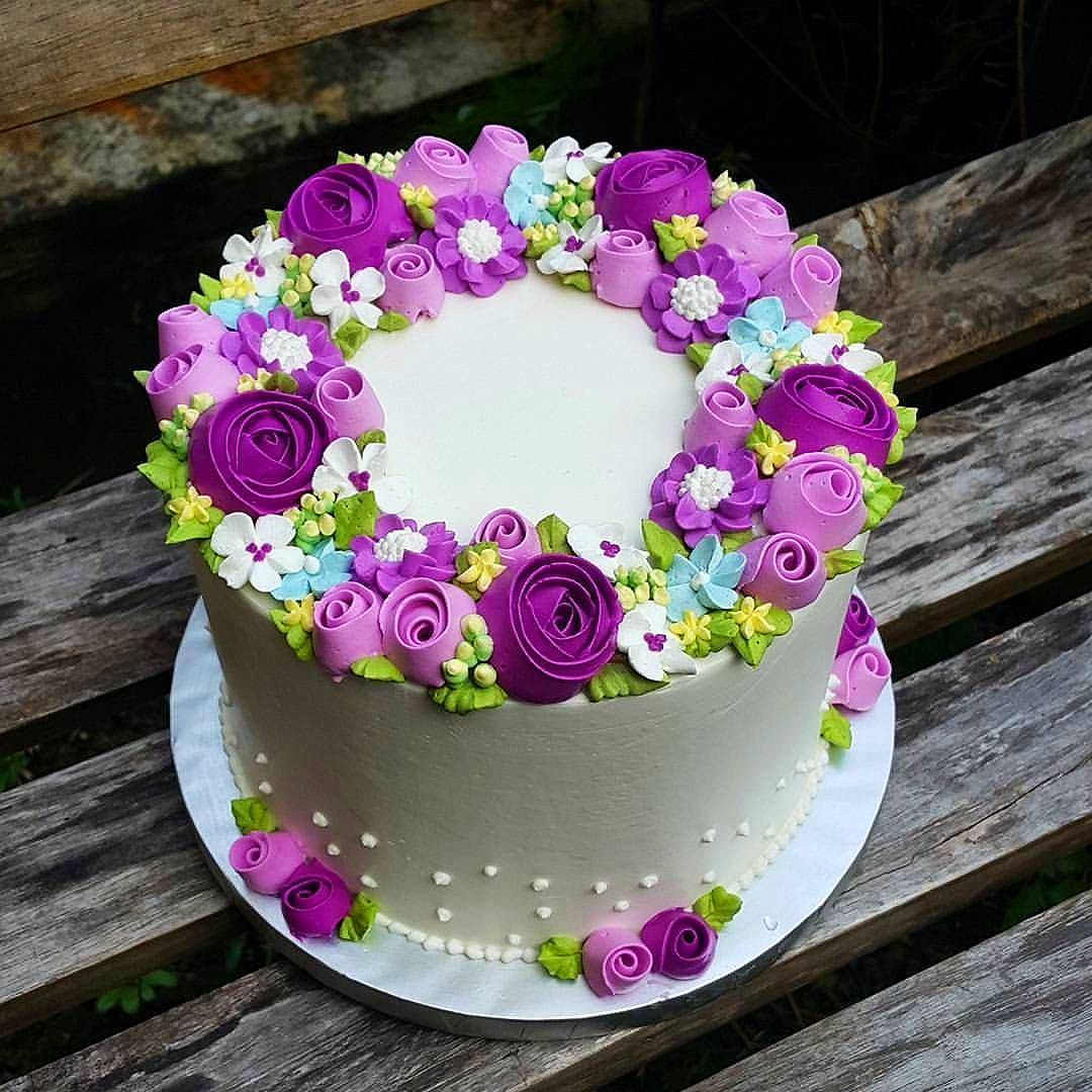 White cake with purple and pink frosting flowers arranged in a wreath on top
