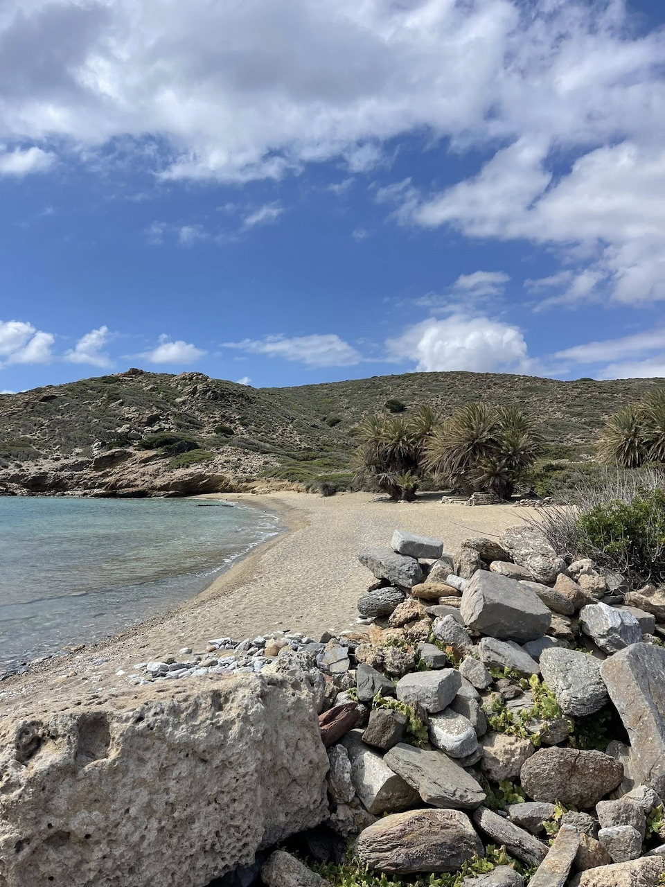 Secluded pebble beach cove with rocky shore, green hills, and blue sky in Greece