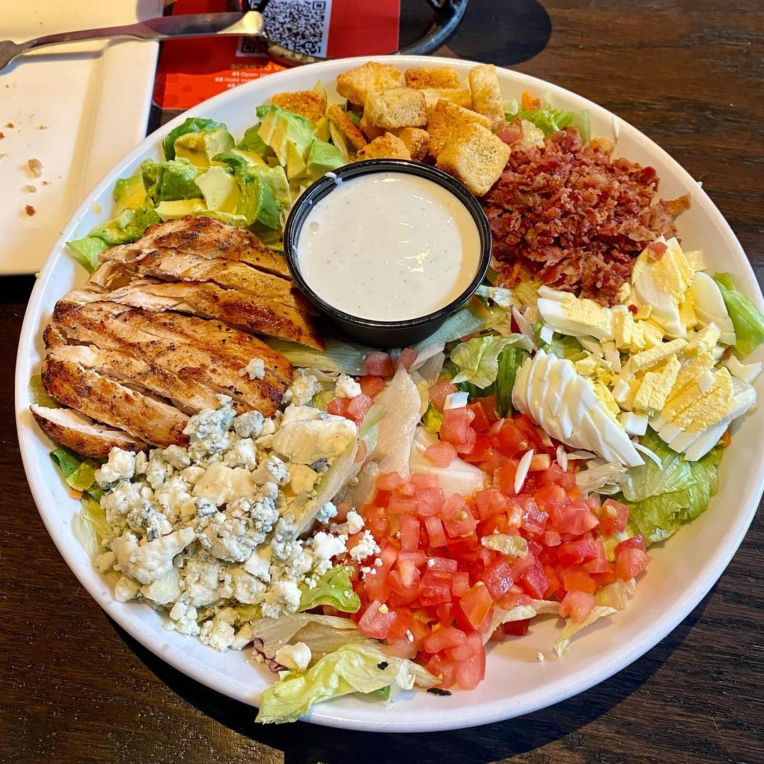 Cobb salad with chicken, bacon, eggs, cheese, tomatoes, and greens arranged in rows with dressing in center