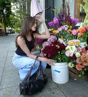 Woman crouching next to vibrant flower buckets on patio