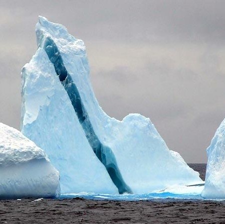 Large blue-white iceberg with deep crevasses floating in dark polar ocean waters