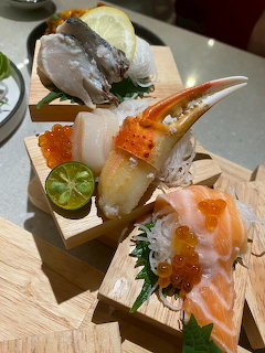 Sashimi platter on wooden blocks with salmon, crab claw, squid, ikura, and oyster