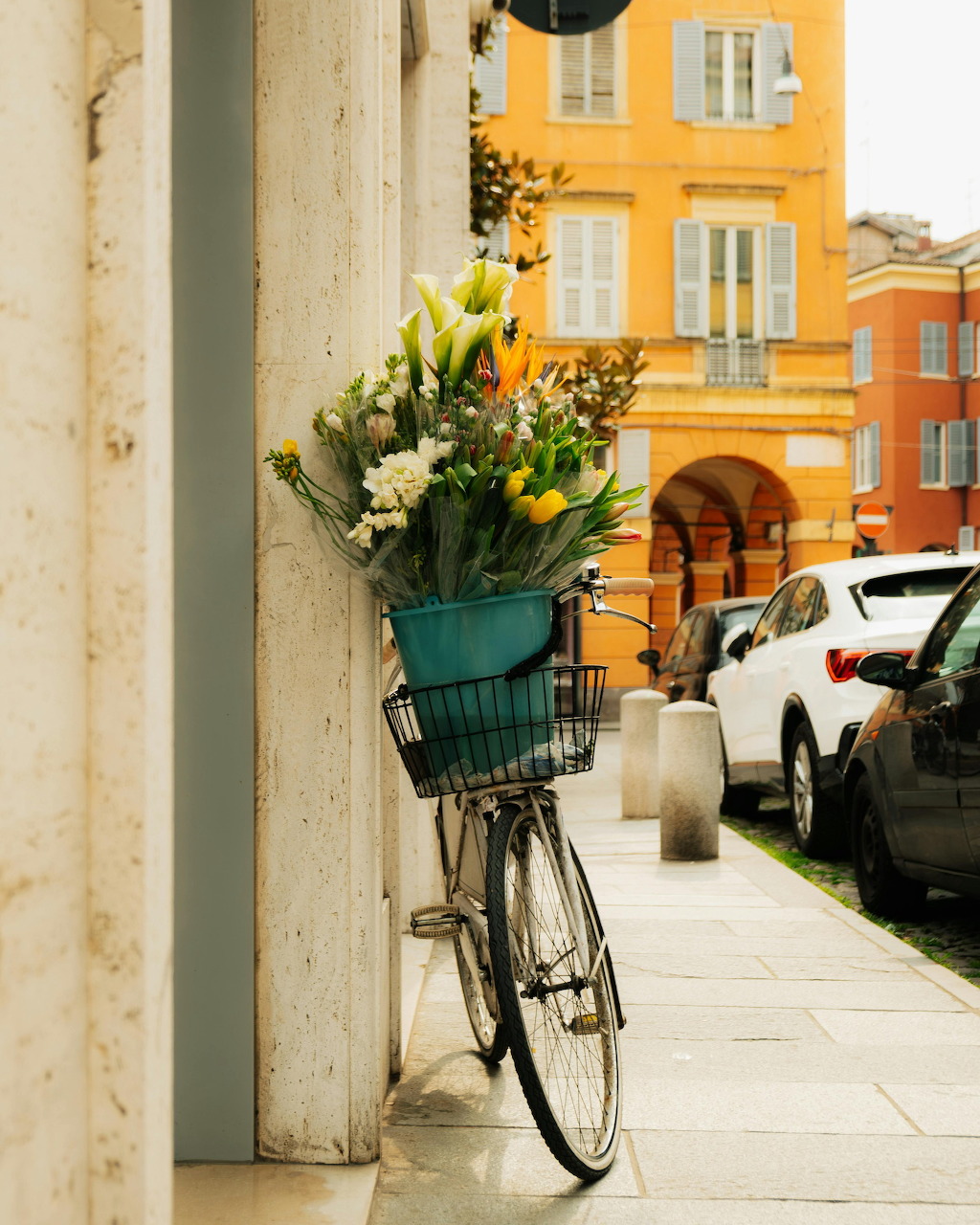 Bicycle with a basket of white and yellow flowers parked against a column on a European street