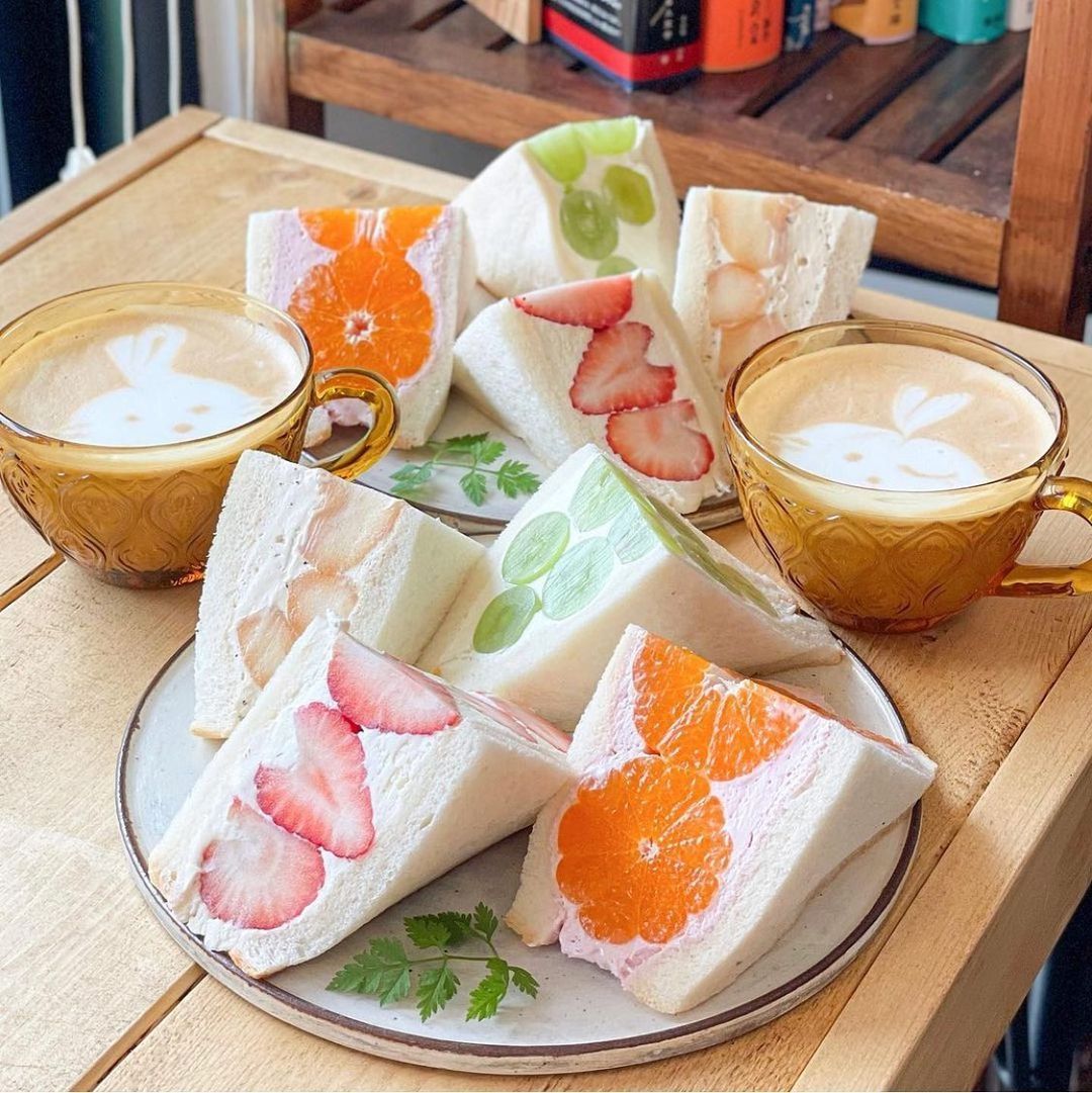 Fruit cream sandwiches on a plate with two cups of latte on a wooden table