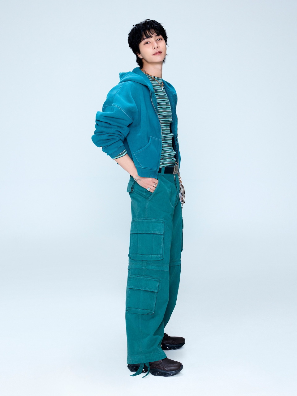 Young Asian man wearing a teal hoodie and matching teal cargo pants posing against a light background