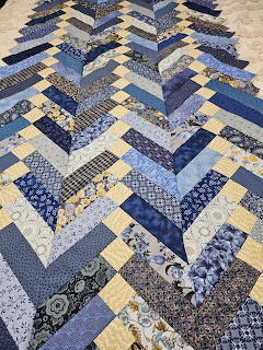 Blue and yellow chevron patchwork quilt with mixed fabric patterns laid outdoors