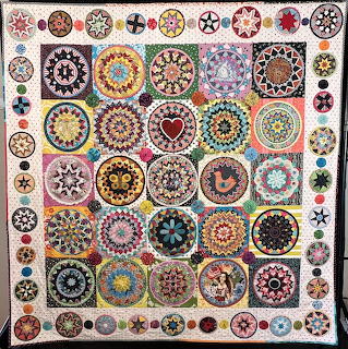 Colorful folk art quilt with circular mandala patterns in grid layout with floral border