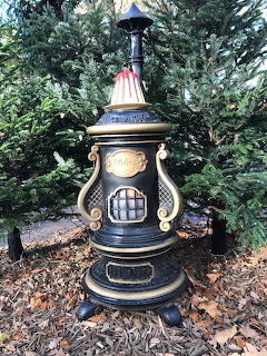 Ornate black and gold garden lantern standing on leaf-covered ground before evergreen shrubs