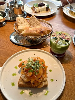 Overhead view of breakfast spread with toast, salmon dishes, matcha drink and various plates on wooden table