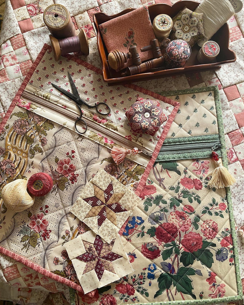 Vintage sewing supplies with floral quilt squares, thread spools, scissors and notions on checkered fabric