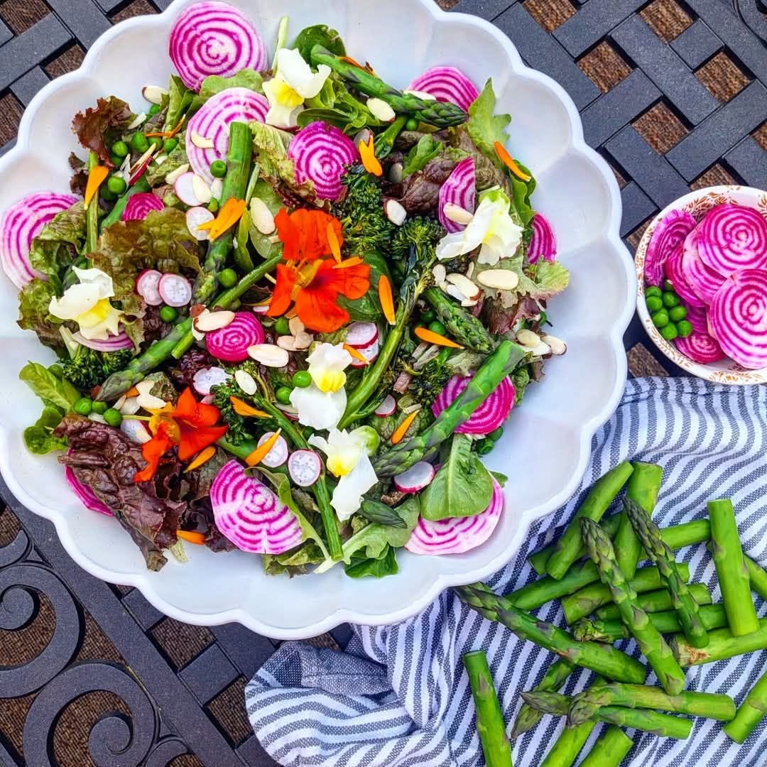 Top view of a colorful salad with edible flowers, sliced radishes, greens, and asparagus