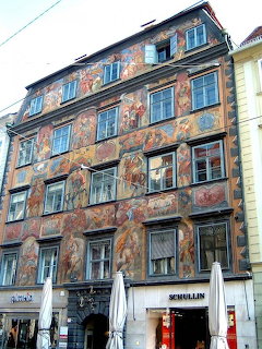 Historic building in Graz with colorful painted frescoes covering the entire facade and shops below