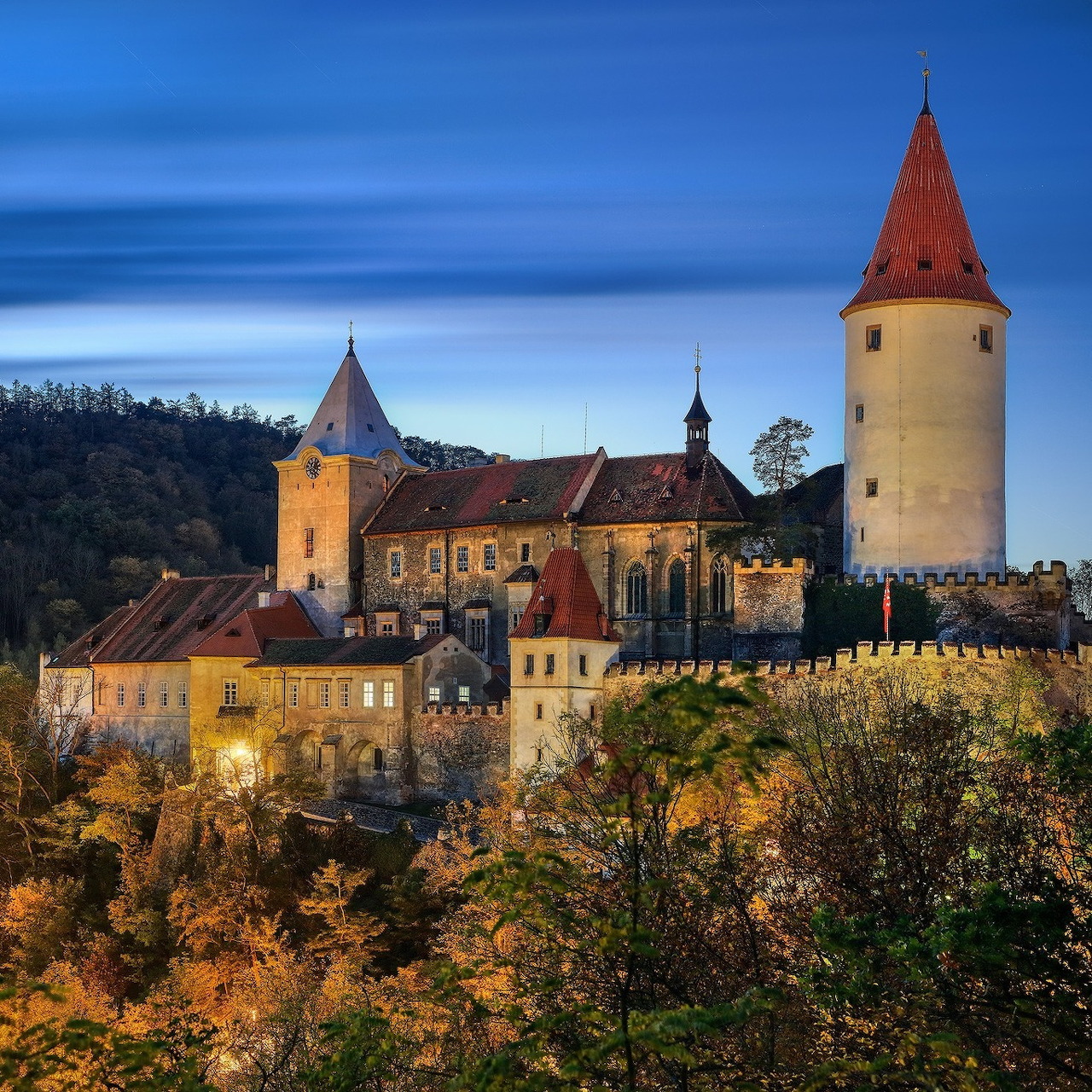 Medieval castle with towers and church at twilight surrounded by autumn trees