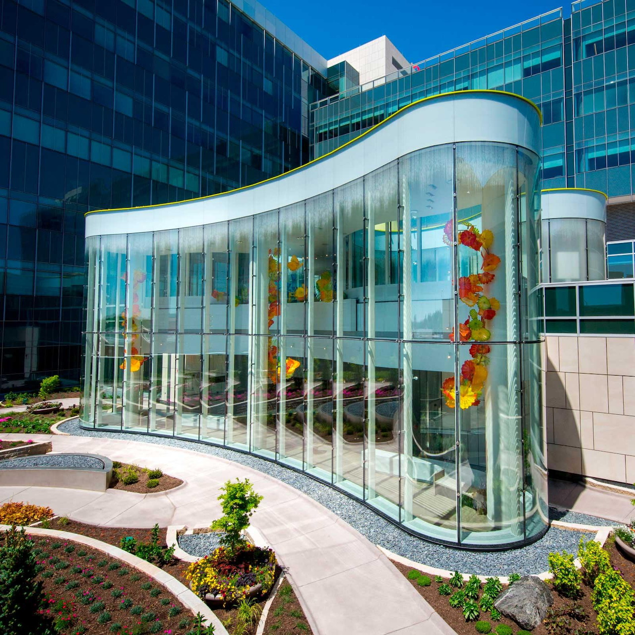 Modern curved glass building entrance with colorful art sculptures in landscaped courtyard
