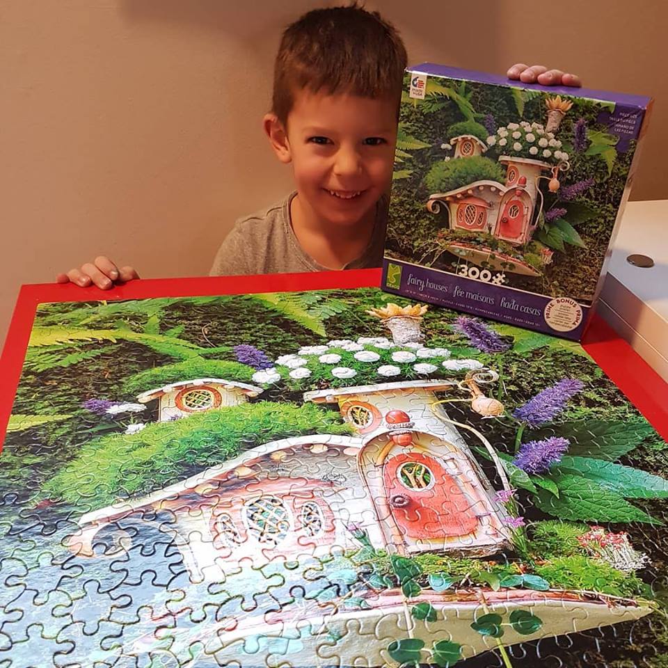 Smiling boy holding a colorful cottage jigsaw puzzle and its box indoors