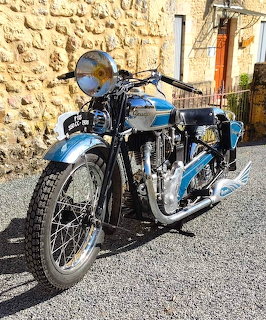 Blue vintage Peugeot motorcycle with chrome engine parked outdoors against stone building