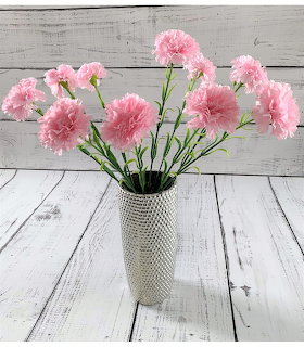 Pink carnations in a textured vase on a white wooden table and rustic plank backdrop.