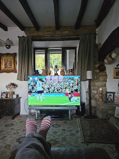 Living room with striped socked feet facing a TV showing a soccer match