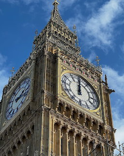 Big Ben clock tower in London with blue sky backdrop, showing detailed Gothic stonework and clock faces