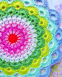 Colorful crocheted mandala with pink center, white, yellow, green and blue rings in a decorative circular pattern