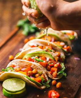 Hand squeezing lime over row of vegetarian tacos filled with colorful vegetables on wooden board