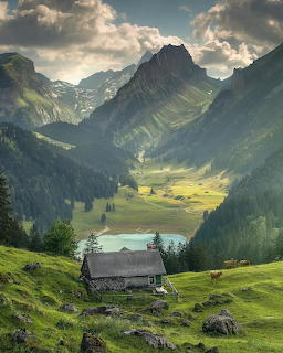 Stone cottage on green hillside with turquoise alpine lake and dramatic mountain peaks in background