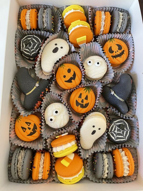 Halloween macarons with pumpkin, ghost, and spider web designs in orange, white, and black colors arranged in a box