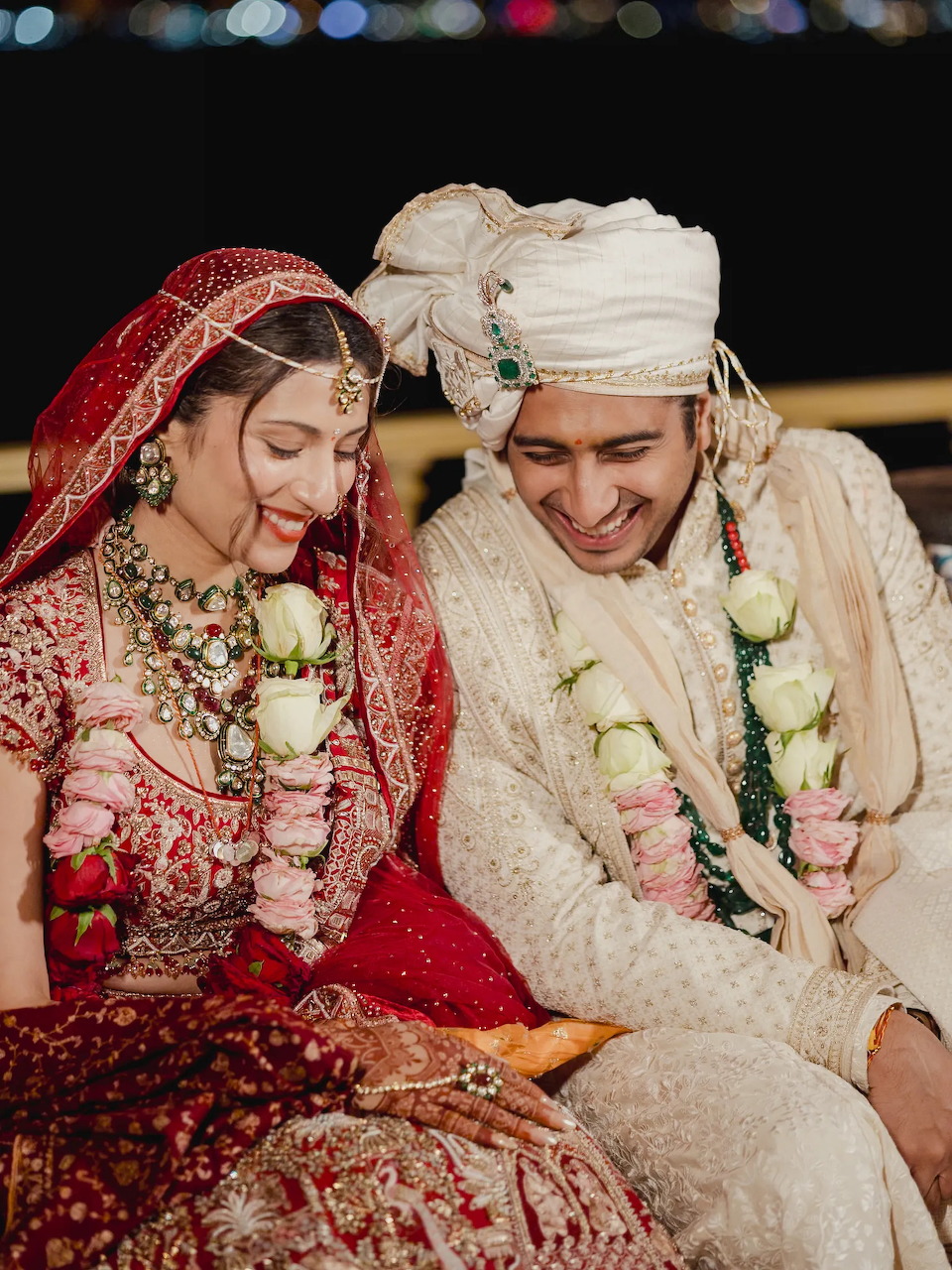 Indian bride in red lehenga and groom in cream sherwani smiling together during wedding ceremony