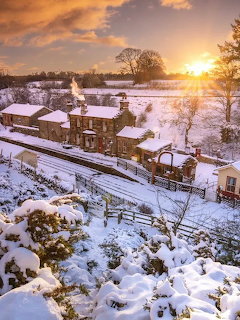 Snow-covered village with stone houses and railway tracks at golden sunset in winter