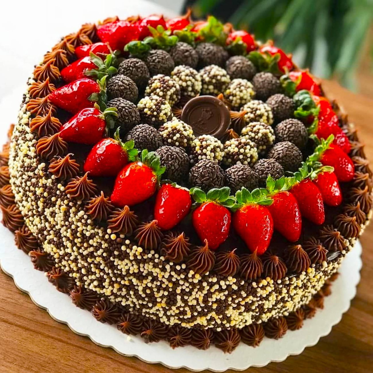 Round chocolate cake decorated with strawberries, blackberries, chocolate truffles, and white pearls in circular pattern
